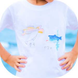 自分が描いた魚の絵のTシャツを着る子ども